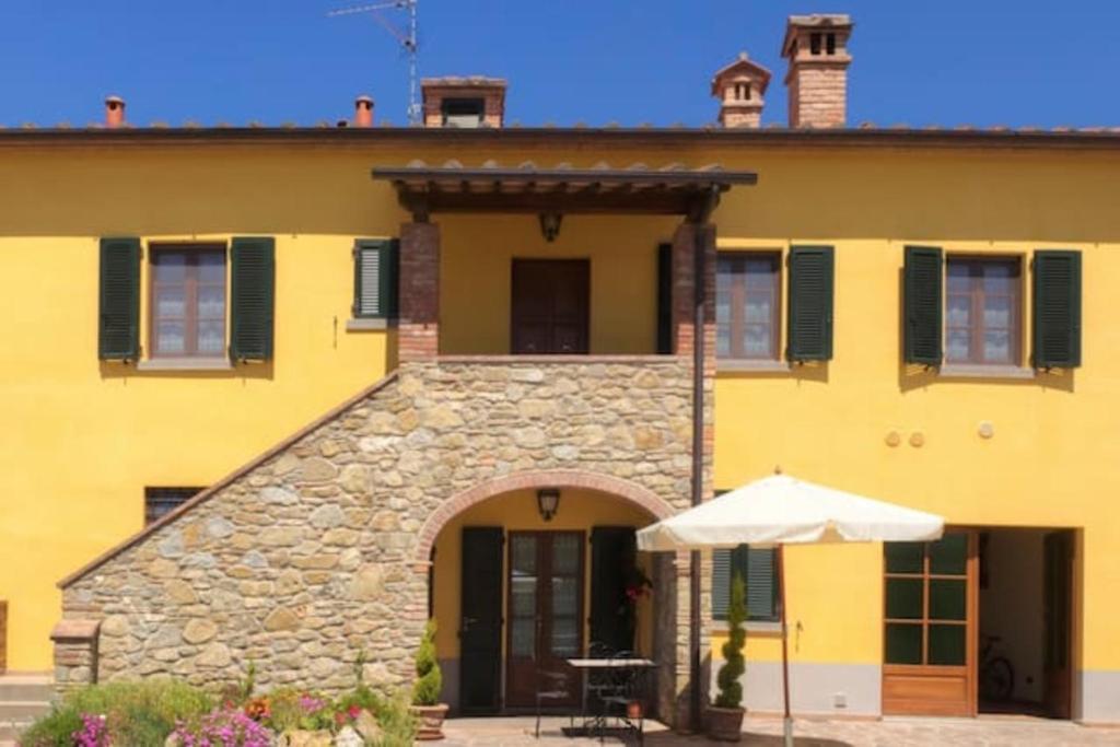 une maison jaune avec un parasol devant elle dans l'établissement Cappannelle Country House Tuscany, à Castiglion Fibocchi