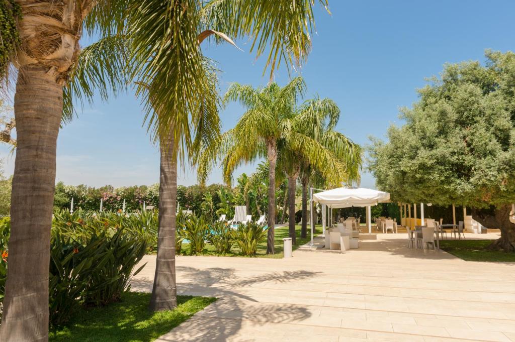 einen Park mit Palmen, Tischen und einem Sonnenschirm in der Unterkunft Life Hotels Kalaonda Resort in Syrakus