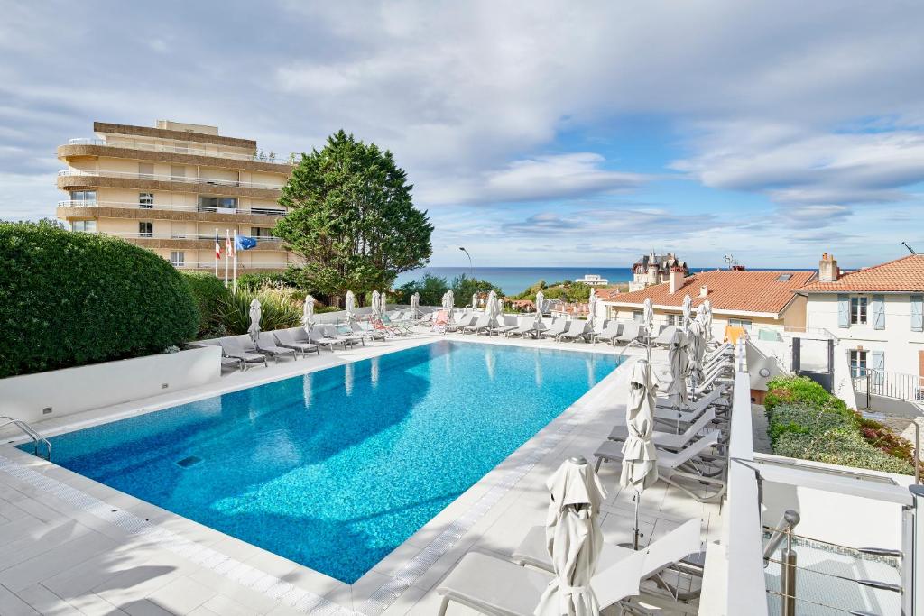 une piscine avec des chaises longues et un bâtiment dans l'établissement Résidence Vacances Bleues Le Grand Large, à Biarritz