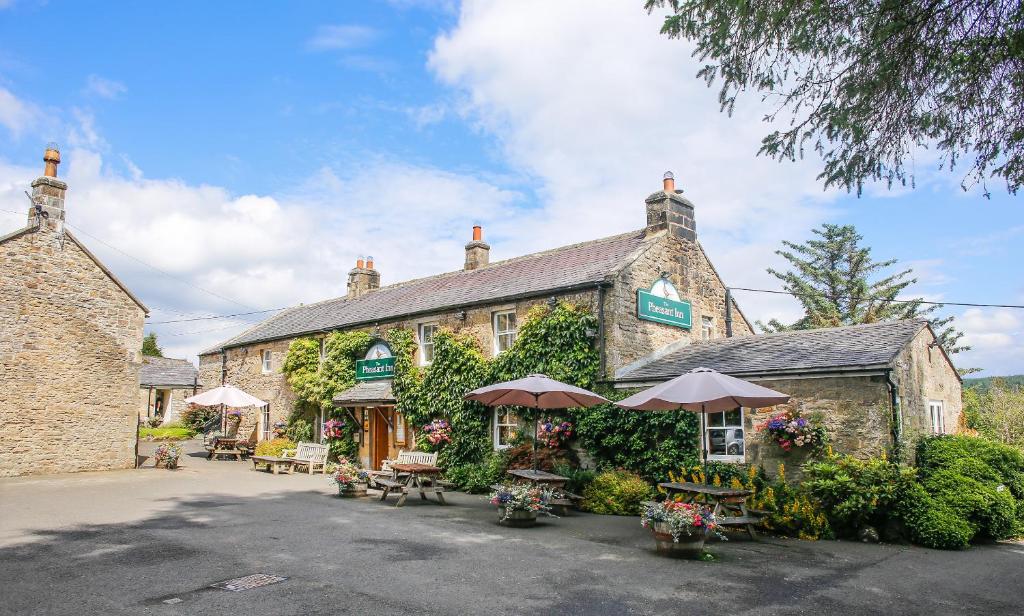 a building with tables and umbrellas in front of it at The Pheasant Inn in Falstone