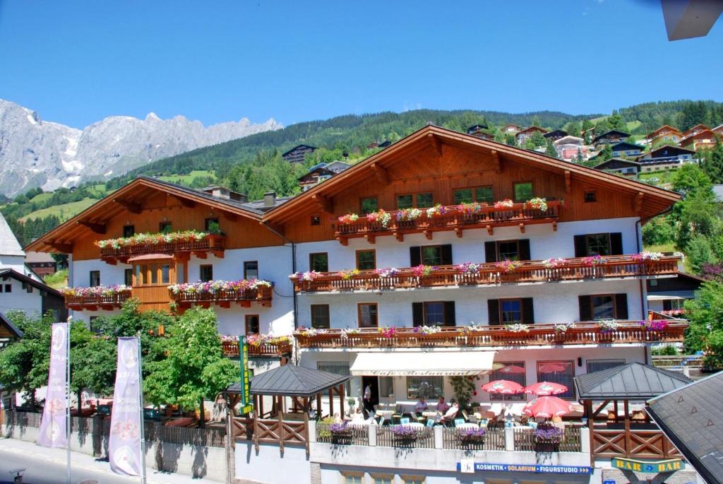 a large building with tables and umbrellas in front of it at Hotel Alpenrose Mühlbach am Hochkönig in Mühlbach am Hochkönig