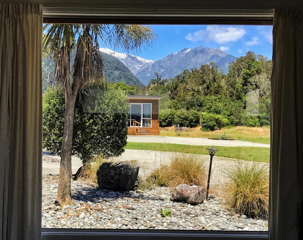 a window view of a house with mountains in the background at Franz Alpine Retreat in Franz Josef