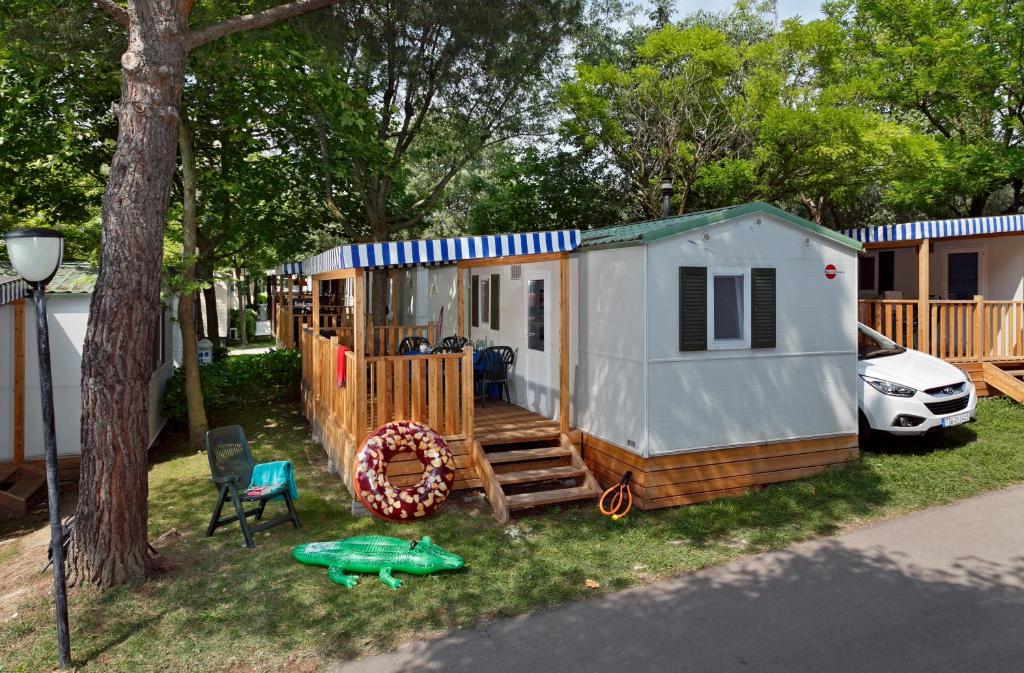 バルドリーノにあるAlbatross Mobile Homes on Camping Cisano & San Vito S. p. A.の木の横の芝生に腰掛けた小屋