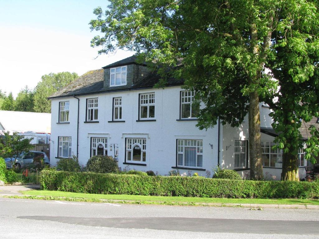 Una casa blanca con un árbol delante. en Meadowcroft Guest House, en Windermere