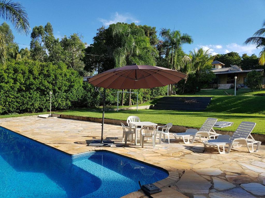 Una mesa y sillas con una sombrilla junto a una piscina. en Rancho Hollywood - Lago de Furnas, en São José da Barra