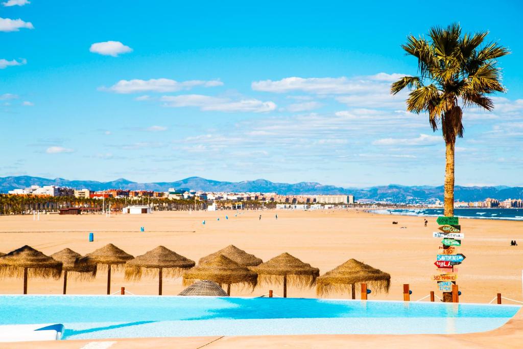 uma praia com guarda-sóis de palha e uma palmeira em Apartment on the beach,pool,WiFi,garage,Valencia em Valência