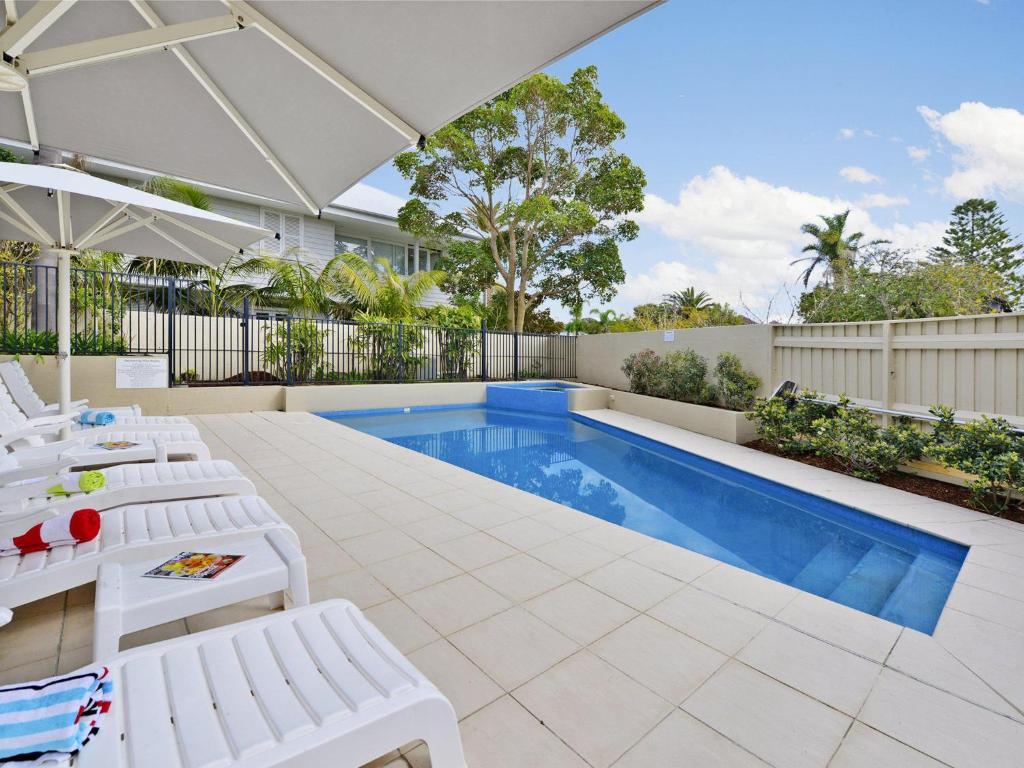 une piscine avec des chaises longues blanches et une piscine dans l'établissement Iluka Twelve at Iluka Resort Apartments, à Palm Beach