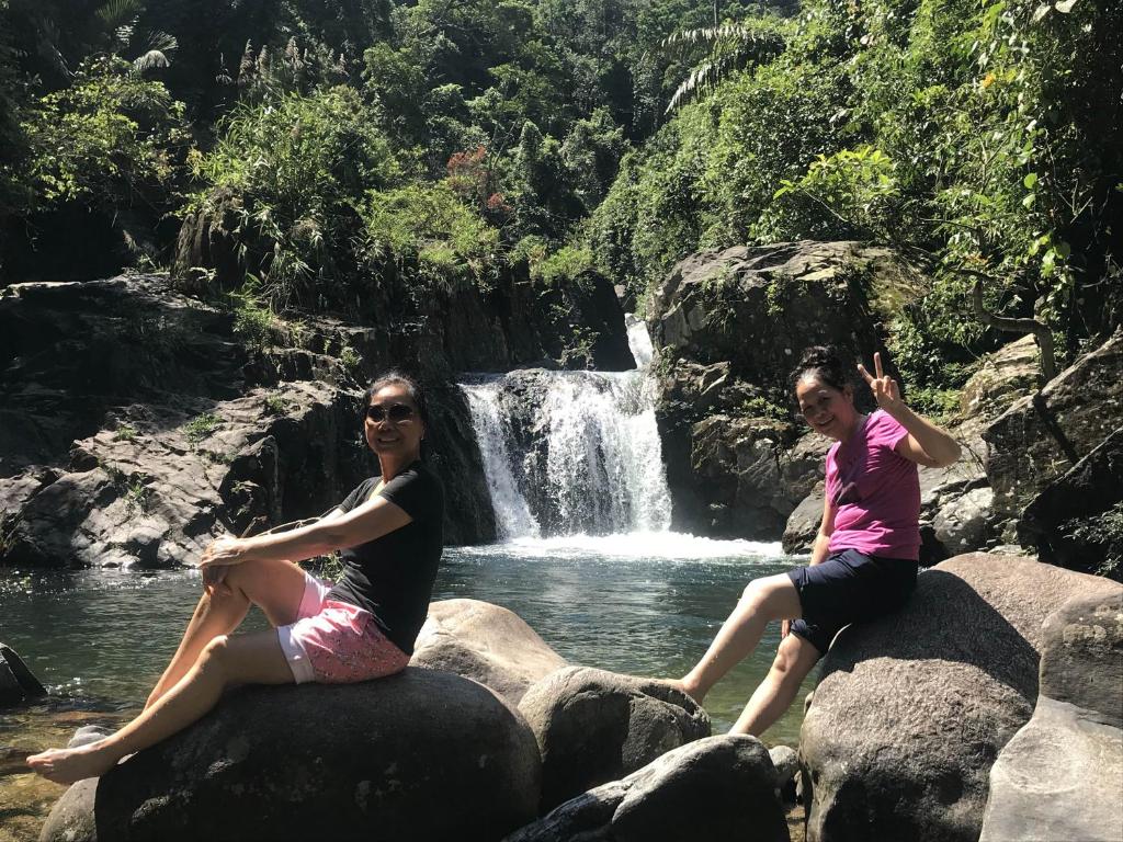 deux femmes assises sur des rochers devant une cascade dans l'établissement Homestay 21& Sweet Yoga House, à PhÆ°á»›c SÆ¡n