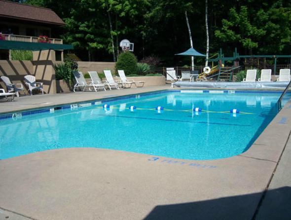 a large swimming pool with blue water and chairs at Tall Pines Motel in Lake George