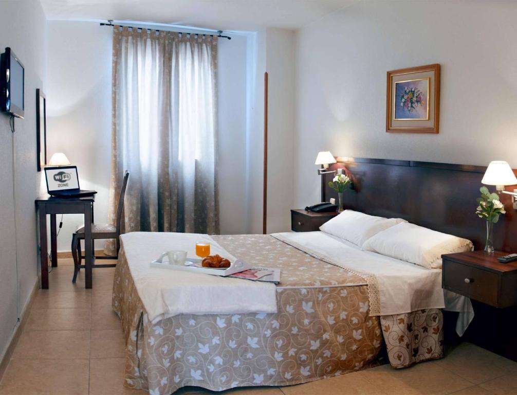 a hotel room with a bed, desk, chair and lamp at Hotel Praderón in San Sebastián de los Reyes