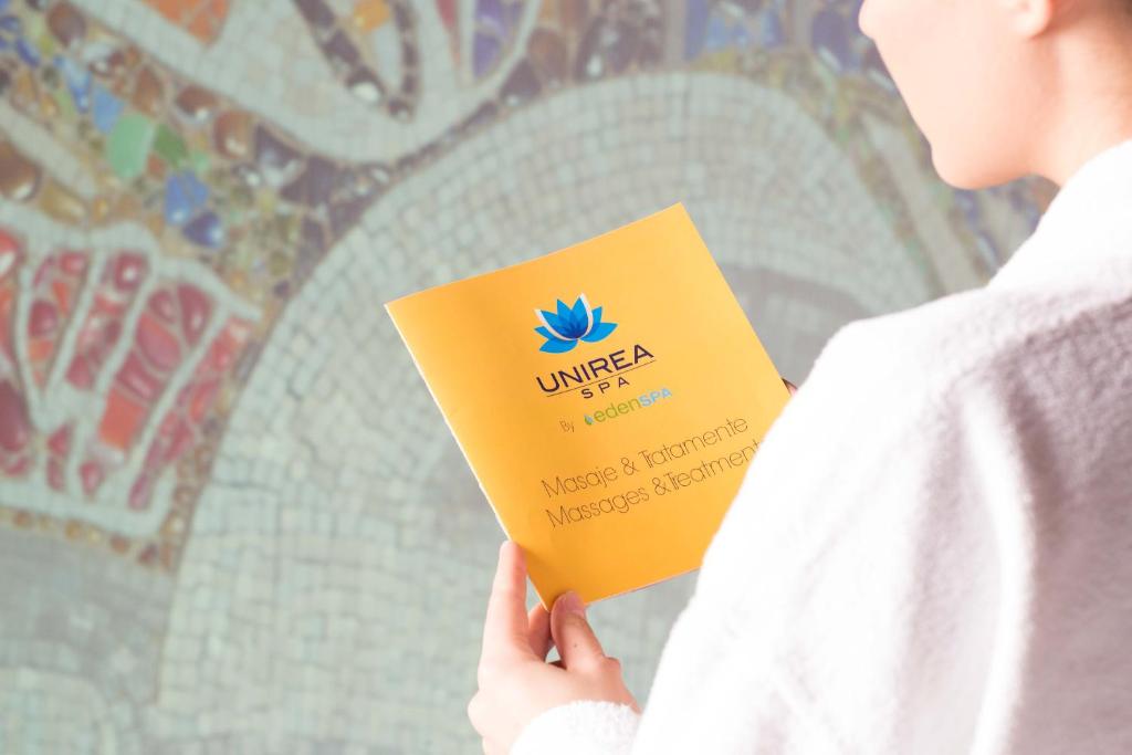a person holding a book in front of a wall at Unirea Hotel & Spa in Iaşi