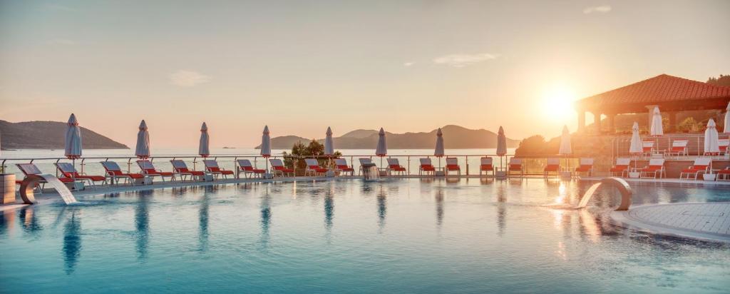 a large swimming pool with chairs and the sun setting at Sun Gardens Dubrovnik in Dubrovnik
