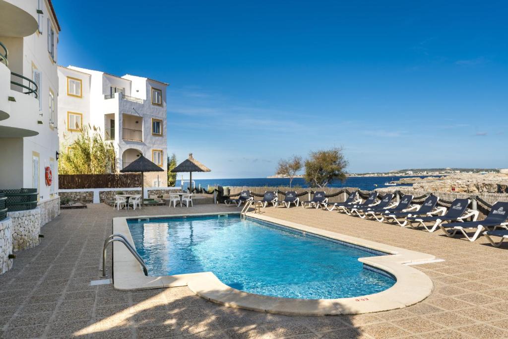 a swimming pool with chairs and the ocean in the background at Apartamentos Sol Ponent in Cala Blanca