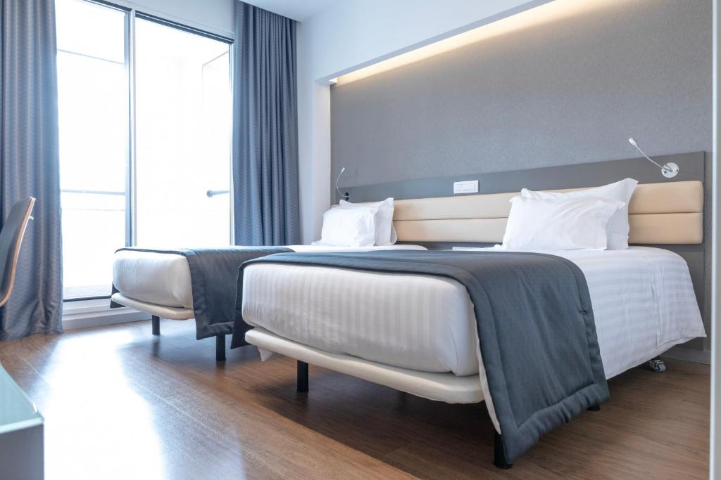 A brighter twin room places two beds beside a tall window and a padded headboard.