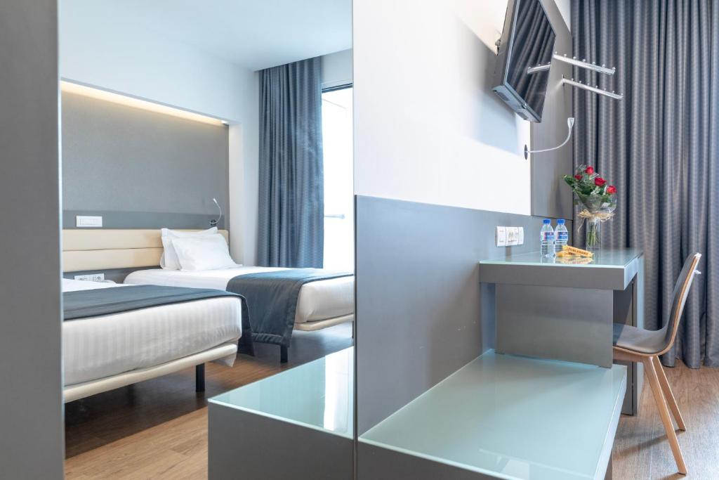 A mirrored bedroom shows a bed, desk, television and bottled water.