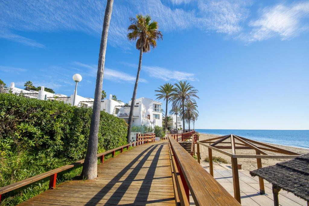a wooden boardwalk leading to the beach with palm trees at Cubo's Apartamento Tarajes La Cala in La Cala de Mijas