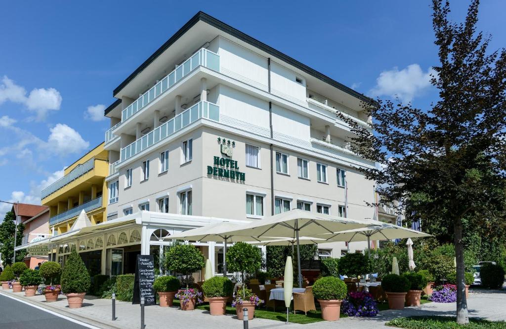um edifício branco com guarda-chuvas à frente em Dermuth Hotels – Hotel Dermuth Pörtschach em Pörtschach am Wörthersee