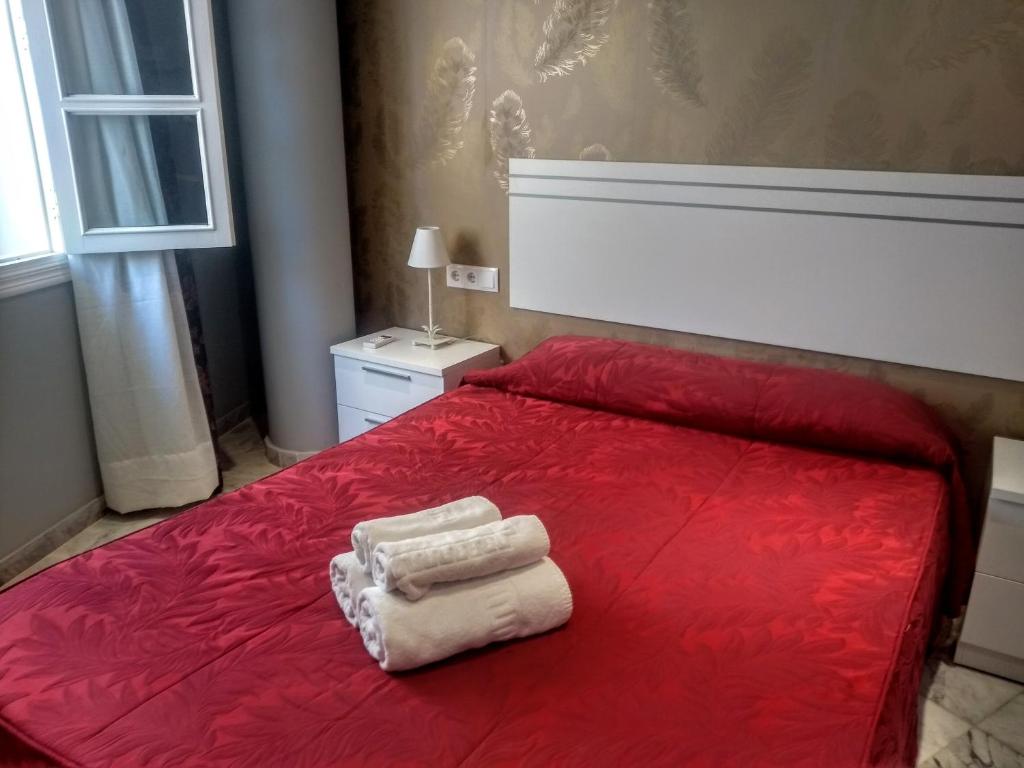 Una cama roja con dos toallas encima. en Apartamentos El Vestuario, en Cádiz