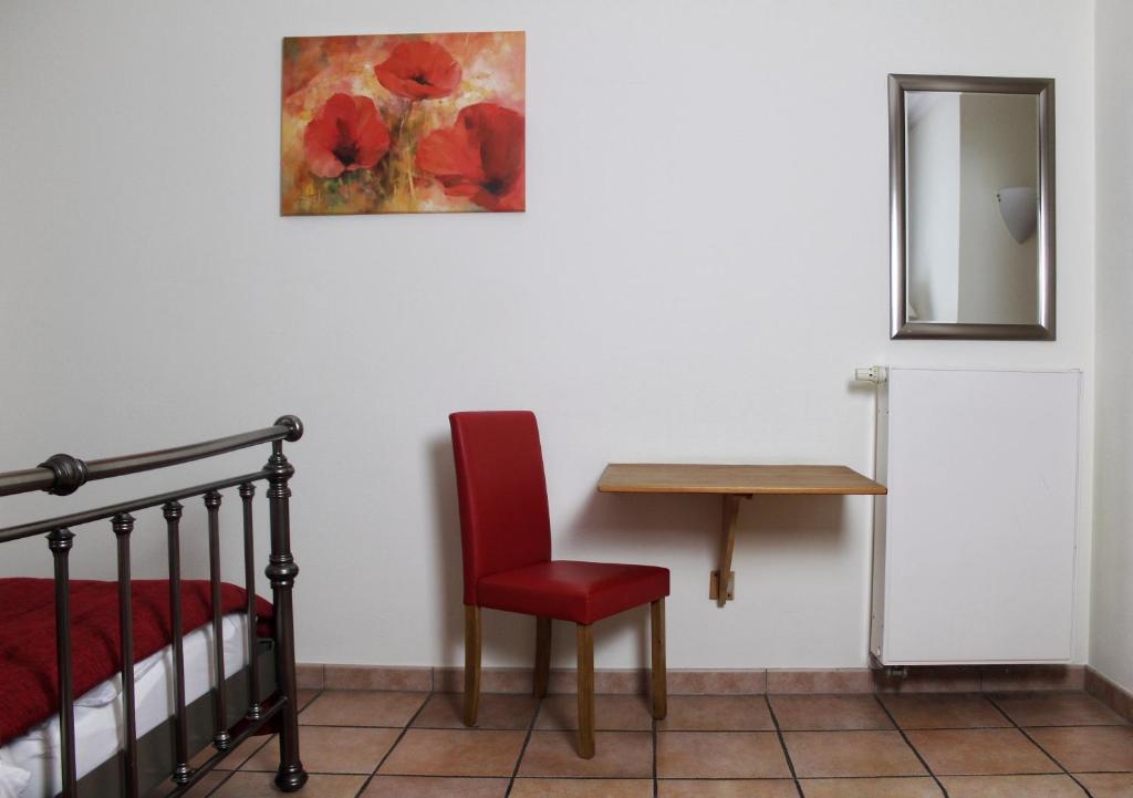 a bedroom with a table and a red chair and a mirror at Akazienhof Hotel & Brauhaus in Cologne