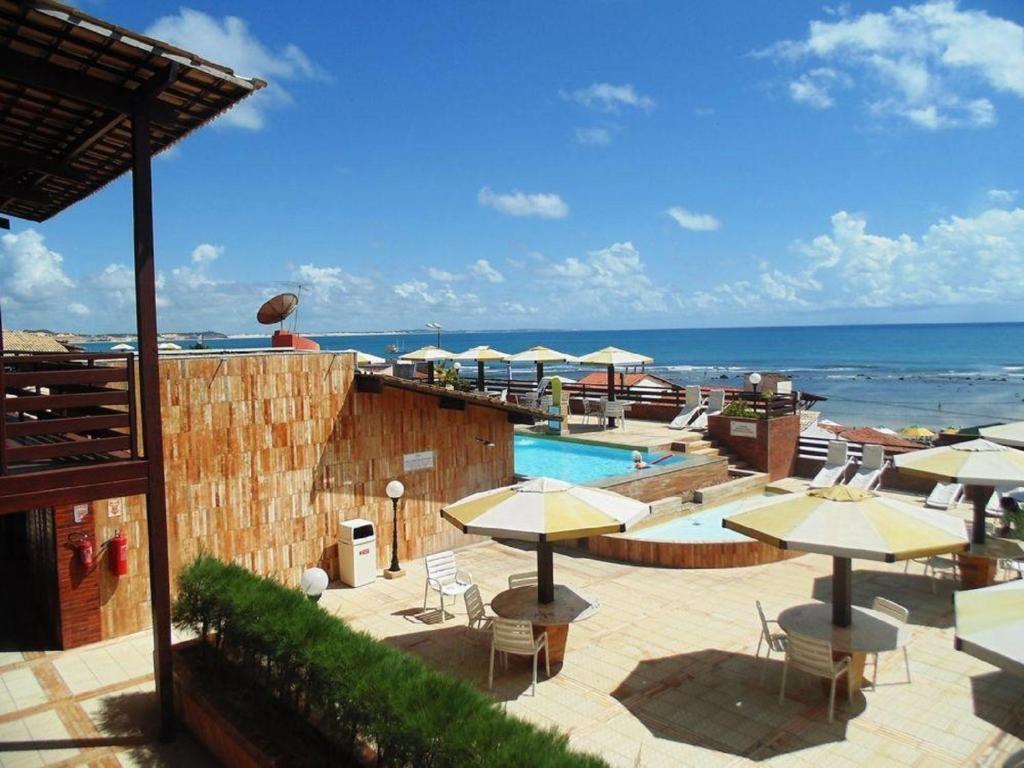 una piscina con mesas y sombrillas junto al océano en Flat Pipa's Ocean a passos da Praia e centro Pipa, en Pipa