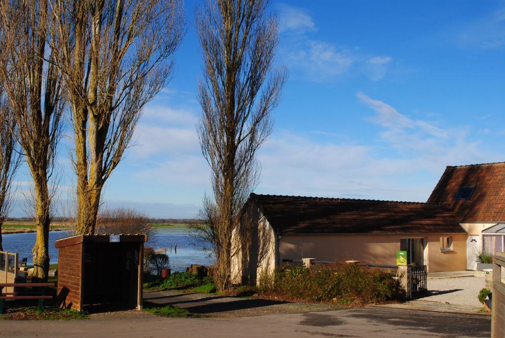 ein Gebäude mit Bäumen und einem See im Hintergrund in der Unterkunft Gite Les Marais de la Douve in Liesville-sur-Douve