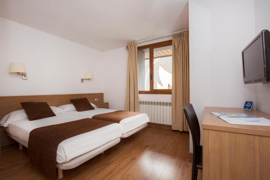 a bedroom with two beds and a desk and a television at Hotel Catalunya Ski in Pas de la Casa