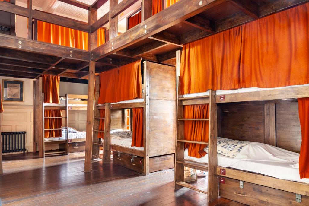a room with three bunk beds with orange curtains at Palmers Lodge Swiss Cottage in London
