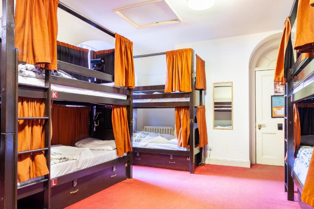 a room with three bunk beds with orange curtains at Palmers Lodge Swiss Cottage in London
