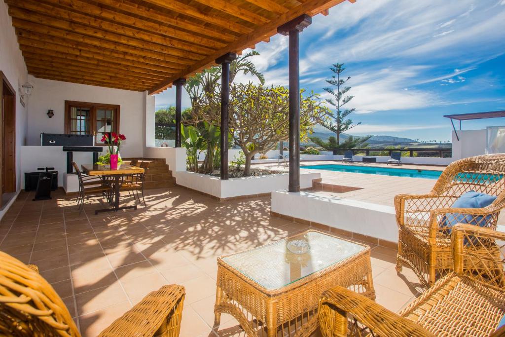 un patio con sillas de mimbre, mesa y piscina en Casa El Quinto, en La Vegueta