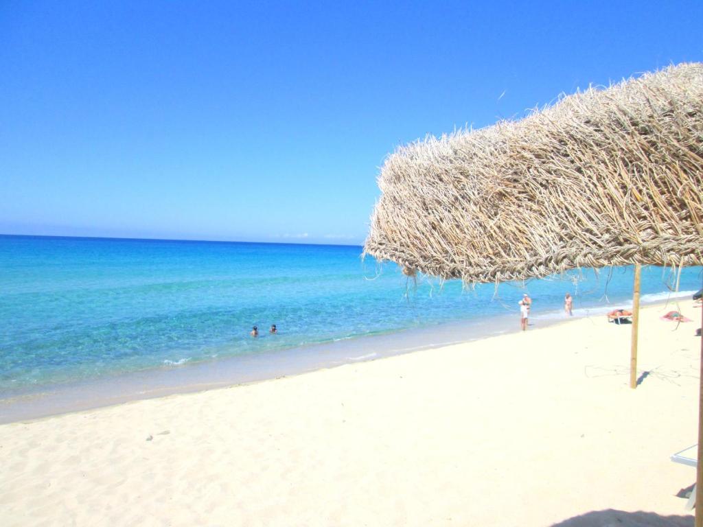 a straw umbrella on a beach with people in the water at Sardinia Yellow House in Solanas