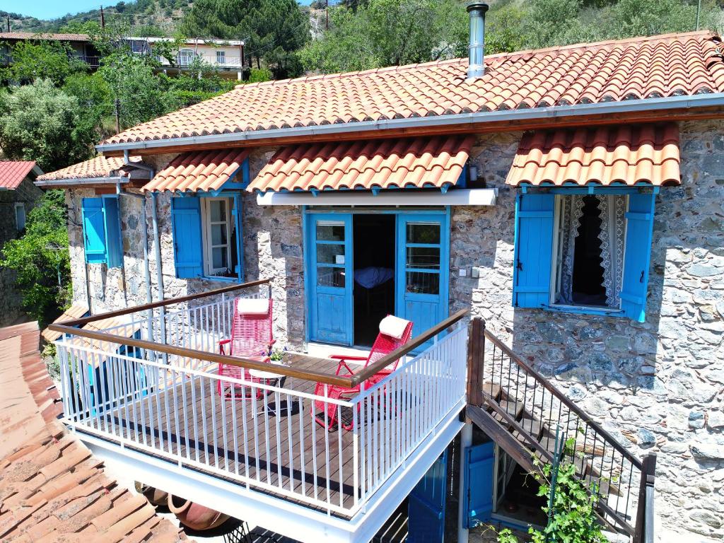 Kalopanayiotis Cottage في كالوبانايوتيس: منزل حجري بأبواب زرقاء وكراسي حمراء على شرفة