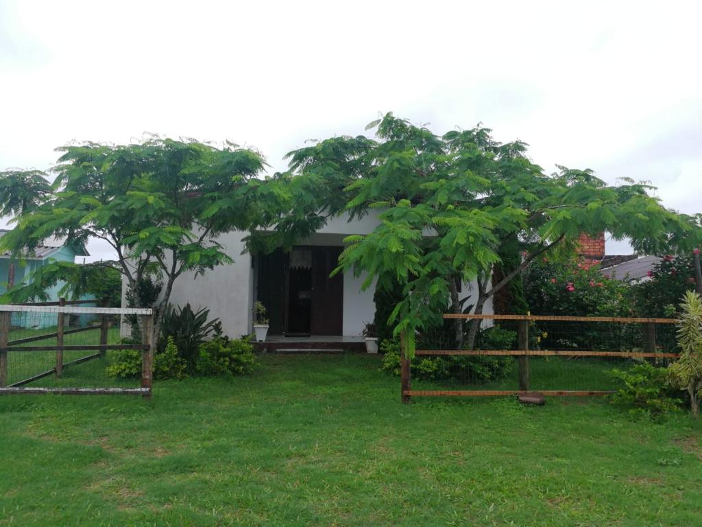 a small white house with trees in the yard at Casa de Praia, baixo custo e boa localização in Xangri-lá