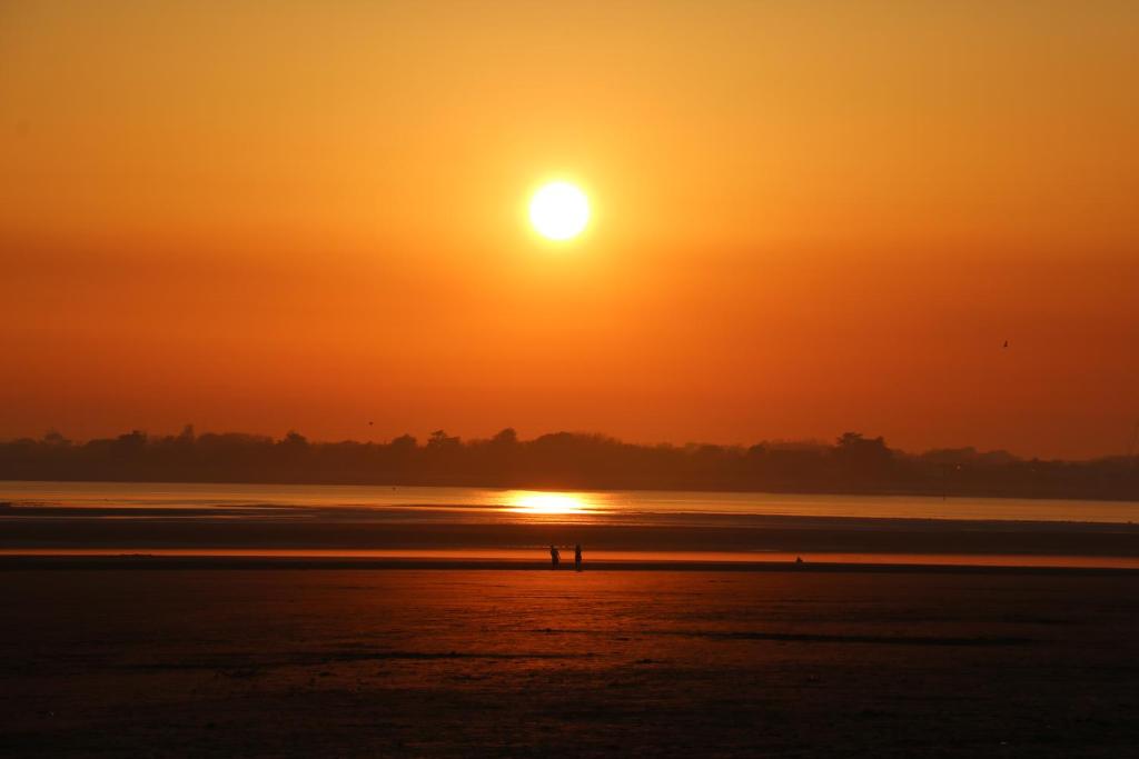 a sunset over the water with two people walking on the beach at Willow House B&B in West Wittering