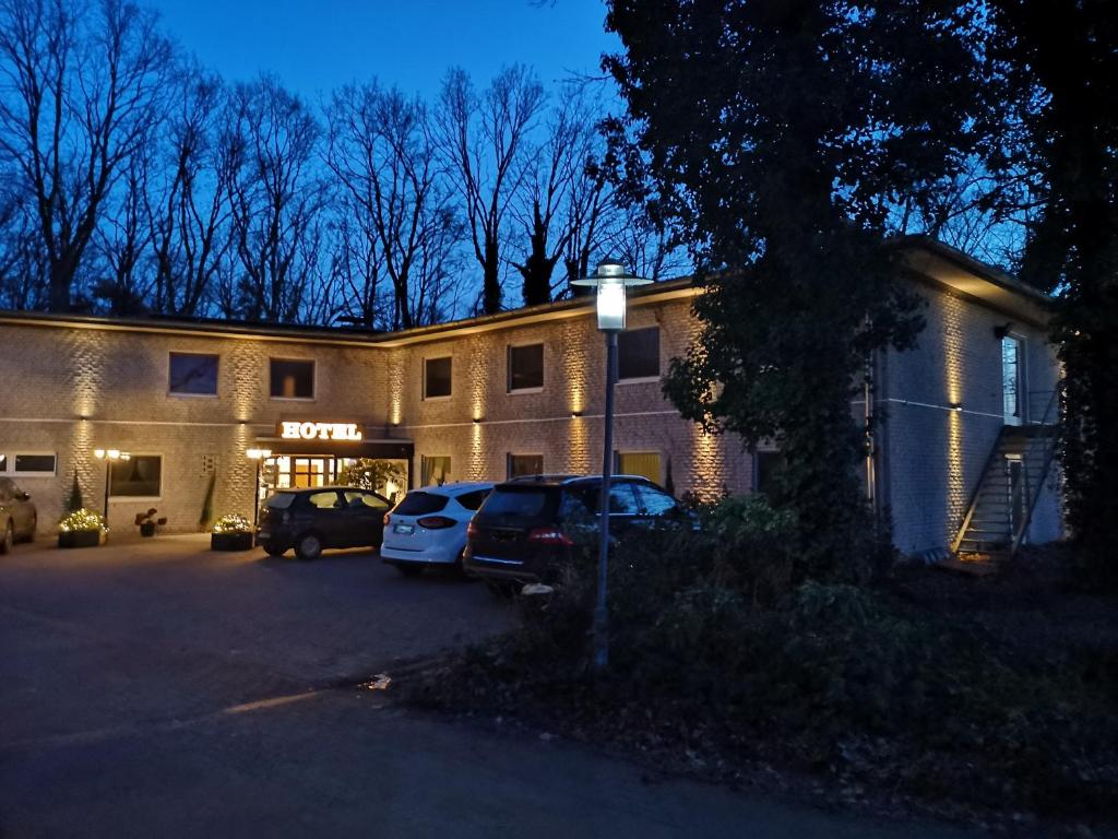 ein Gebäude mit zwei Autos auf einem Parkplatz in der Unterkunft Hotel am Springhorstsee in Großburgwedel