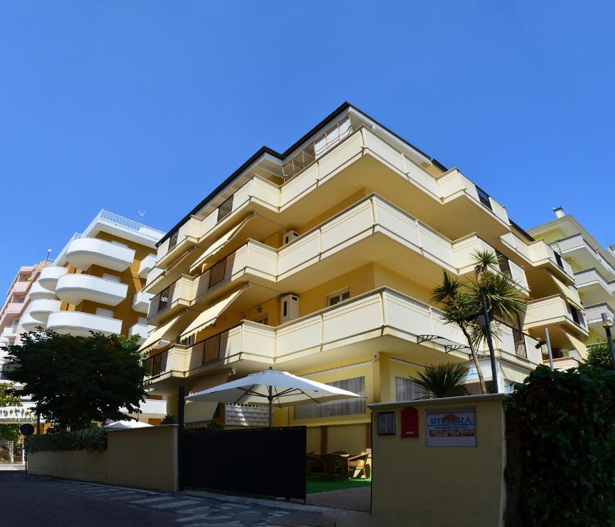 アルバ・アドリアティカにあるResidence Rivieraの傘が目の前にある大きな黄色の建物