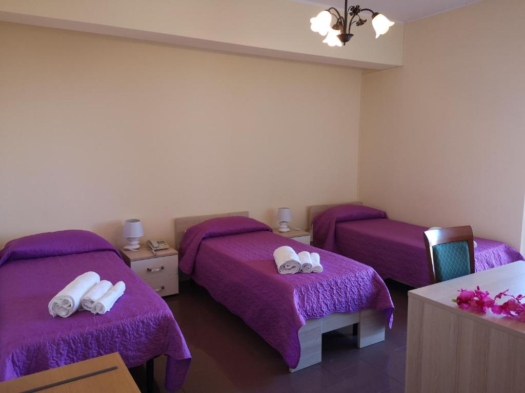 Zimmer mit 3 Betten und lila Bettwäsche in der Unterkunft Grand Hotel Aspromonte in Delianuova