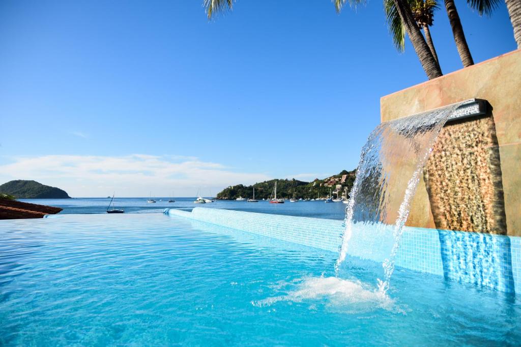 a swimming pool with a fountain in front of the ocean at Arena Suites in Zihuatanejo