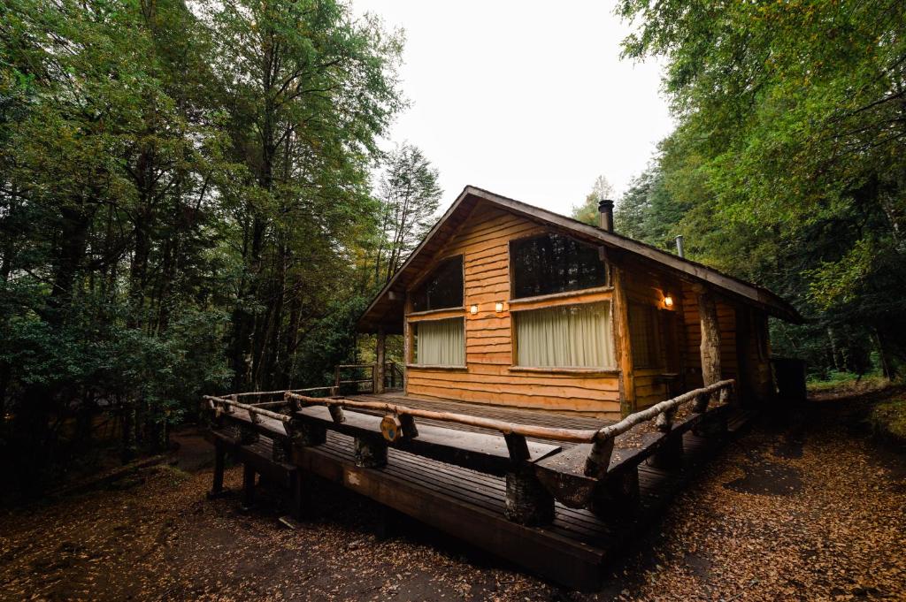 een houten hut in het bos met een veranda bij Huilo Huilo Cabañas del Bosque in Huilo Huilo