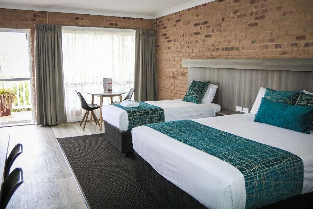 a hotel room with two beds and a table at The Club Motor Inn Chinchilla in Chinchilla