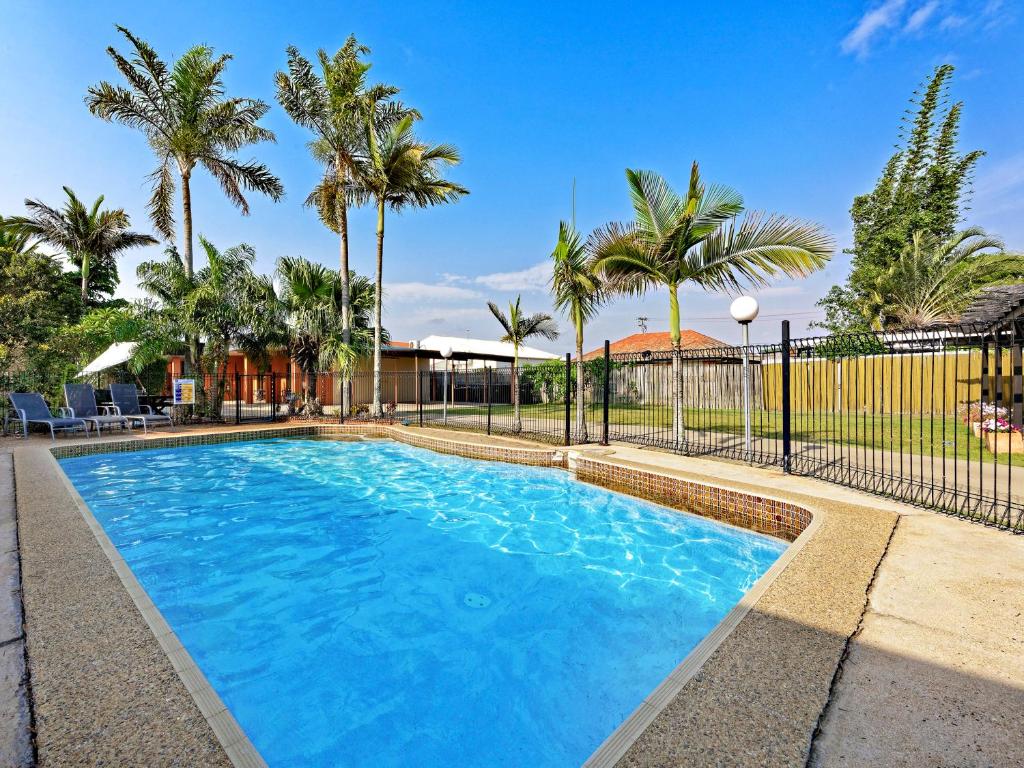a swimming pool with a fence and palm trees at Riviera Motel Bundaberg in Bundaberg