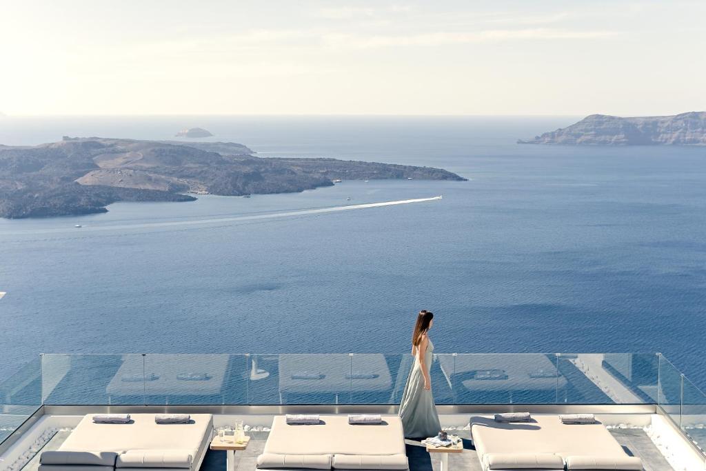 Una donna in piedi su un balcone che guarda l'oceano di Agali Houses a Firostefani