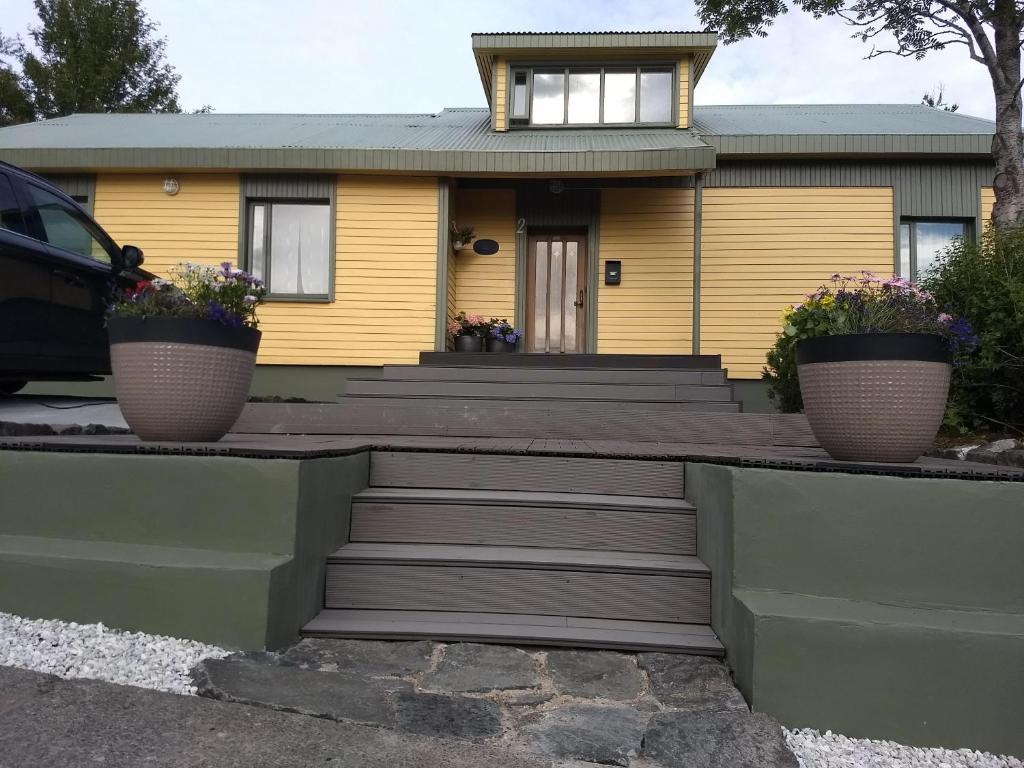 een geel huis met twee bloempotten ervoor bij Reydarfjordur Apartment in Reyðarfjörður