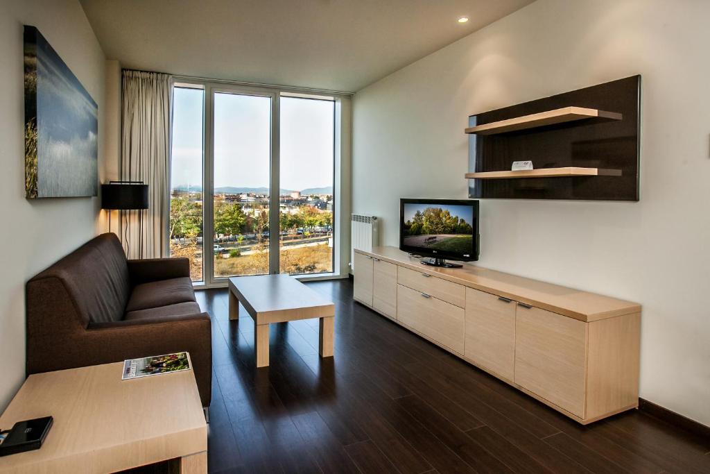 sala de estar con sofá, TV y mesa en Sercotel Jardines de Uleta Suites, en Vitoria-Gasteiz