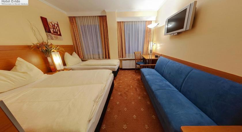Habitación de hotel con 2 camas y sofá azul en Evido Rooms, en Salzburgo