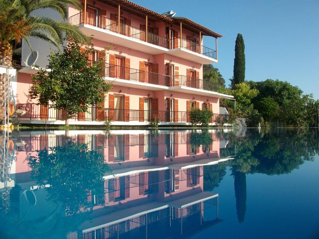 een roze gebouw met een reflectie in het water bij Aronis Apartments in Benitses