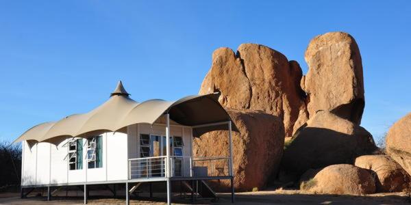 a white house with a roof next to some rocks at Spitzkoppen Lodge in Usakos