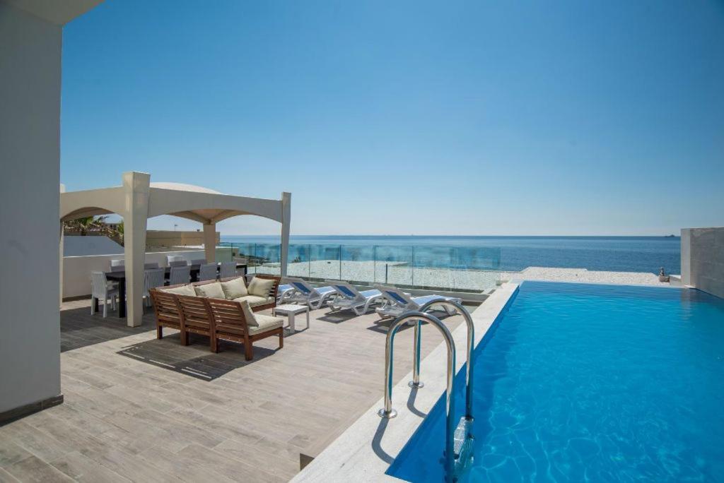 a pool with chairs and a gazebo next to the ocean at The Sea-Bank Villa Apartments in Marsaskala