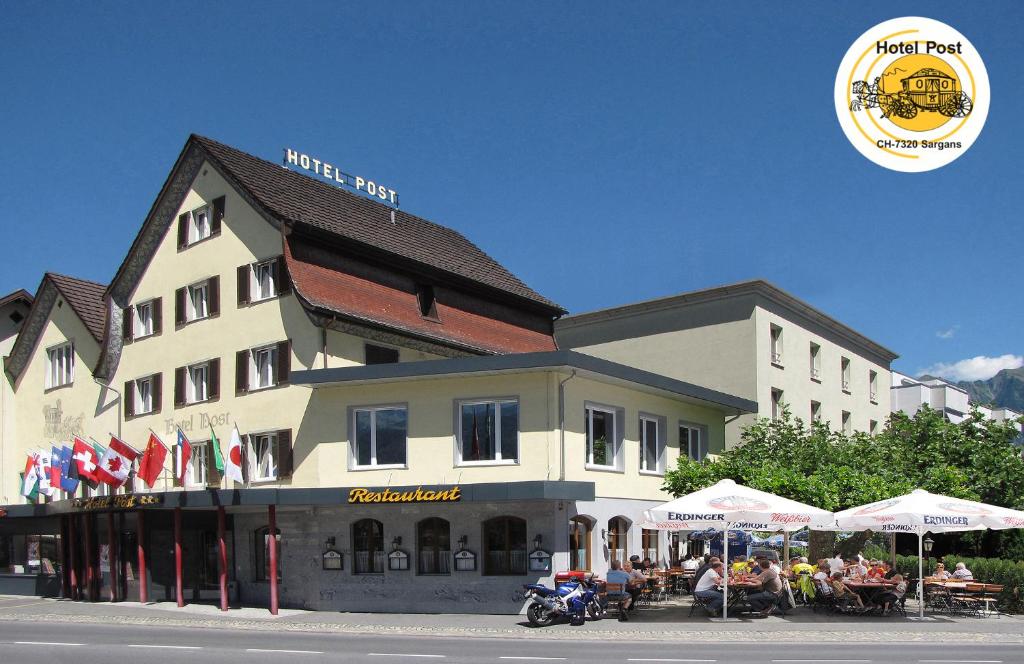 un grand bâtiment avec des personnes assises à l'extérieur dans l'établissement Hotel Post, à Sargans