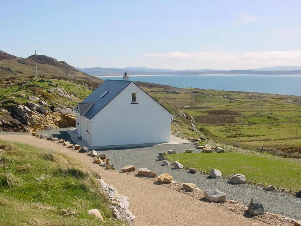 a white barn on a hill next to a body of water at Crohy Cottage in Donegal