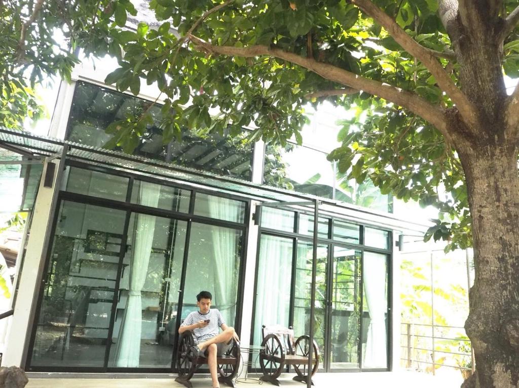 a man sitting on a bench in front of a building at Bann Rai Klai Weang Homestay in Ban Muang Chum